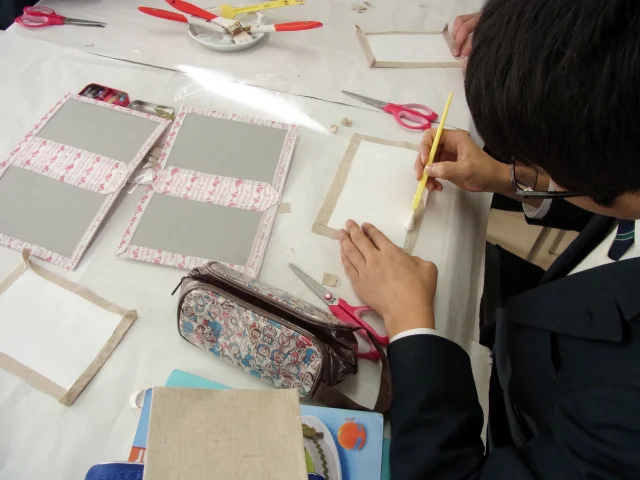 家庭科教材の導入事例：中学2年生の家庭科授業にてカルトナージュのノートカバーを約4時間かけて作成する生徒たちの様子：ノリの貼り付け工程を進める生徒の様子