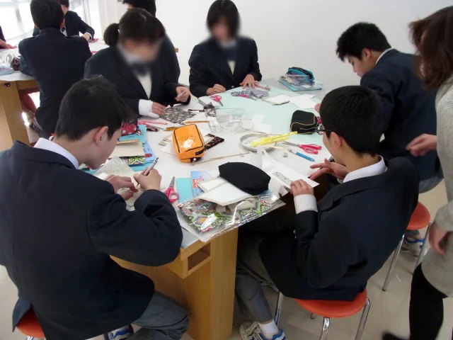 家庭科教材の導入事例：中学2年生の家庭科授業にてカルトナージュのノートカバーを約4時間かけて作成する生徒たちの様子：生徒同士で相談しながら制作を進めている様子の写真